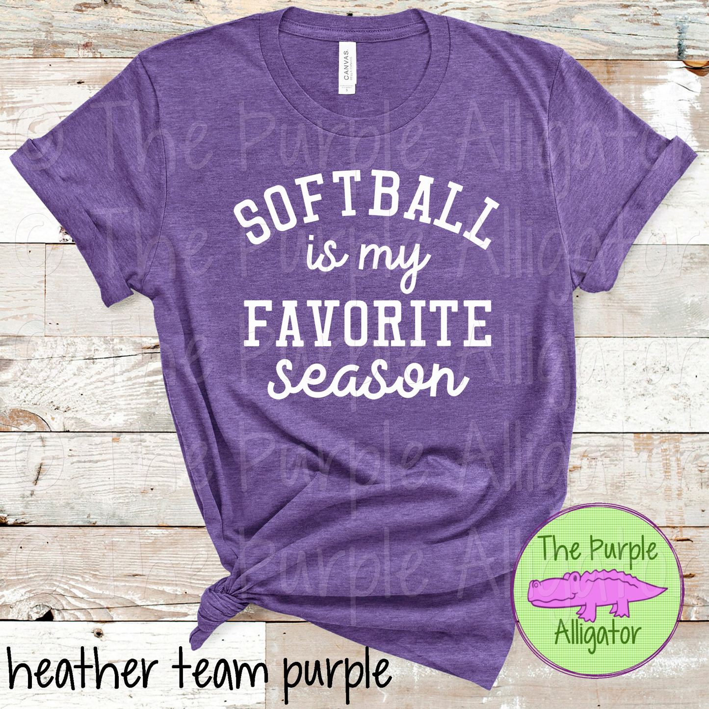 A purple t-shirt with the text 'SOFTBALL IS MY FAVORITE SEASON' printed on the front, displayed on a wooden background. The image also includes a logo of The Purple Alligator.
